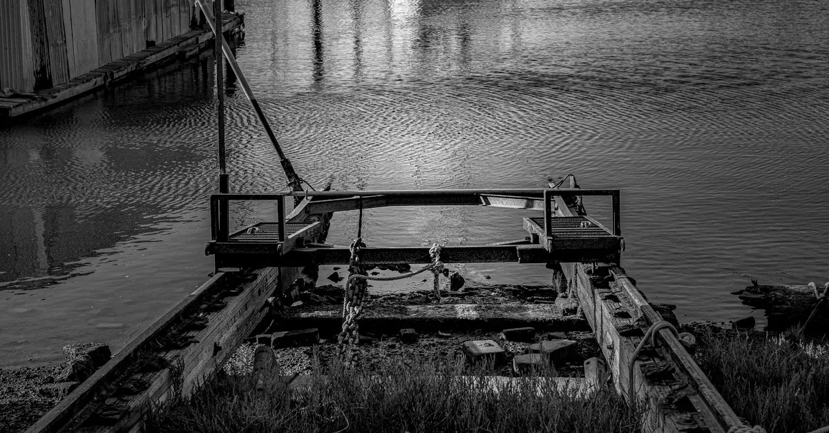Een verroeste, verlaten scheepshelling in stil havenwater bij avondlicht