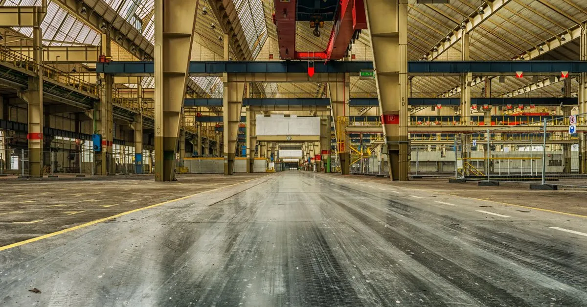 Een lege industriële hal met stalen kolommen en een rijstrook op de vloer, verlicht door hoge ramen